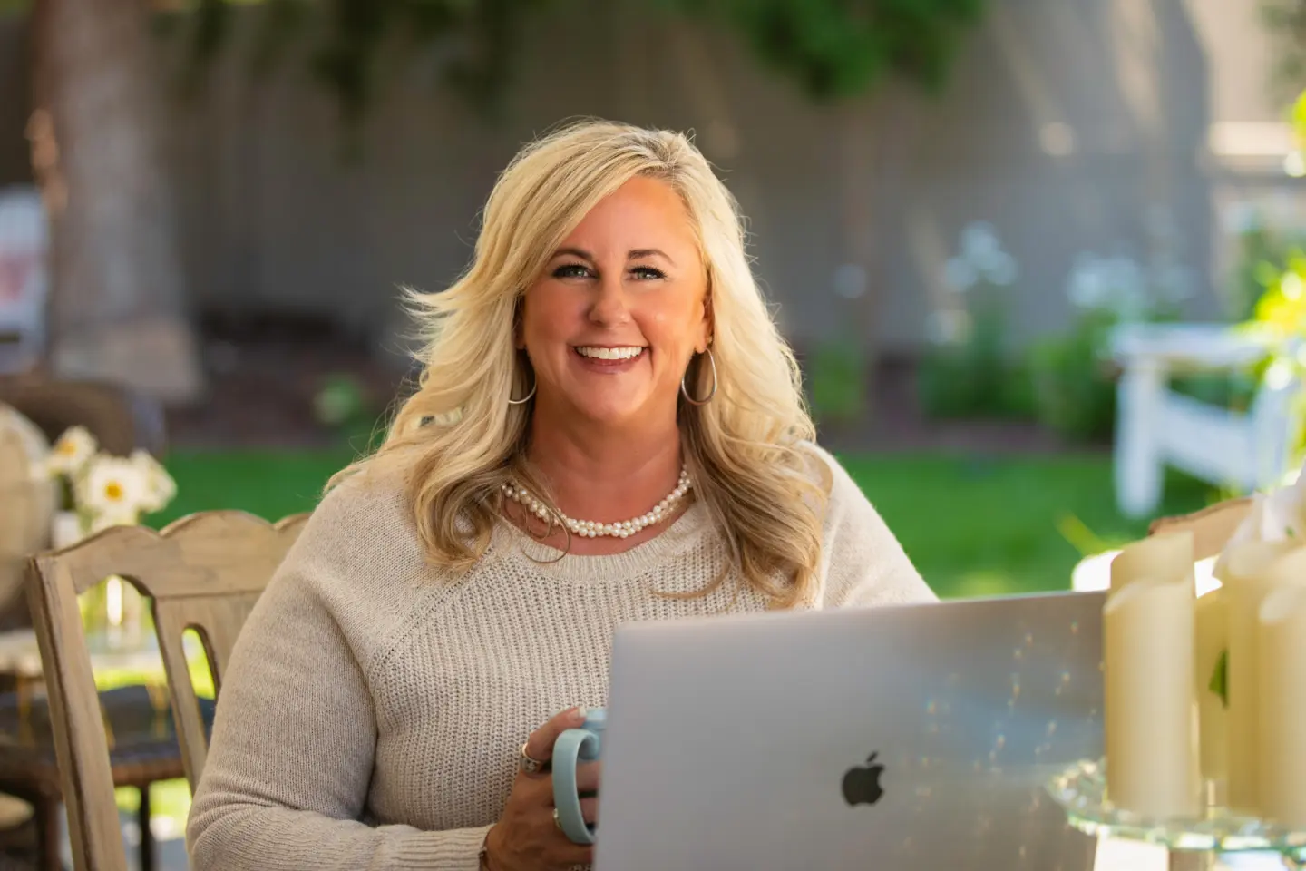Candra smiling at her garden table with a laptop and coffee